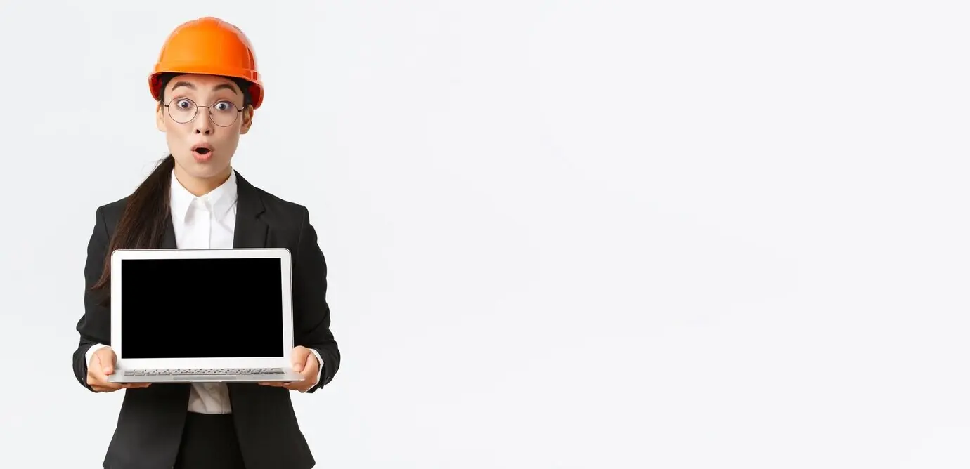 Beeindruckte und begeisterte asiatische Ingenieurin und Industrietechnikerin im Schutzhelm und Anzug zeigt erstaunliche Ergebnisse in einem Diagramm und präsentiert mit erstaunter Miene den Laptopbildschirm vor weißem Hintergrund.